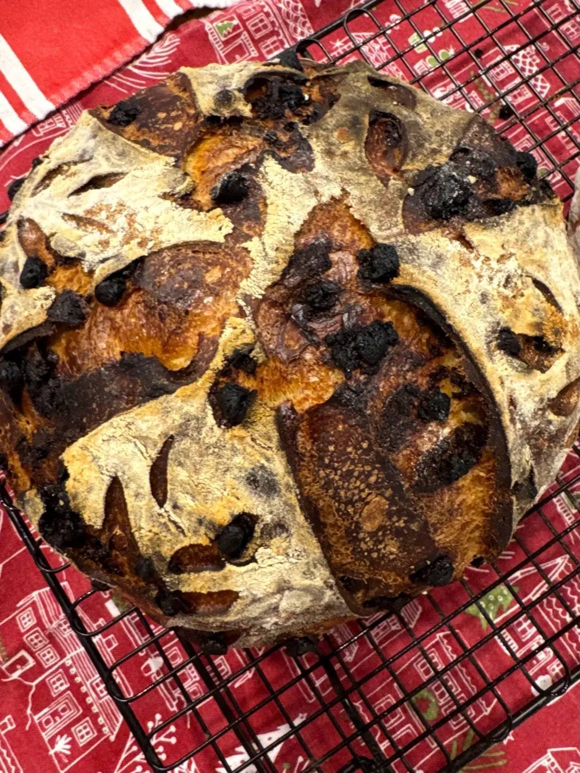 A rustic loaf of bread with a dark, cracked crust cooling on a wire rack.